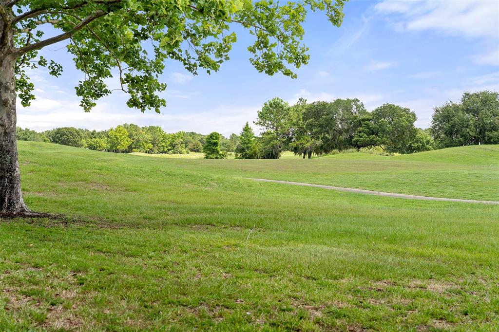 A view of a grassy golf course fairway with trees and a paved path — 7134 FIVE OAKS DR UNIT 4B, ST CLOUD, FL