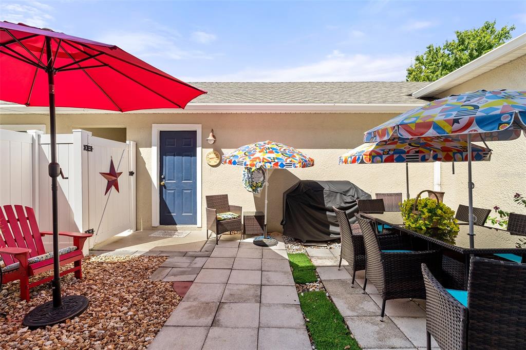A patio features a dining set, a red Adirondack chair, and several colorful umbrellas — 7134 FIVE OAKS DR UNIT 4B, ST CLOUD, FL
