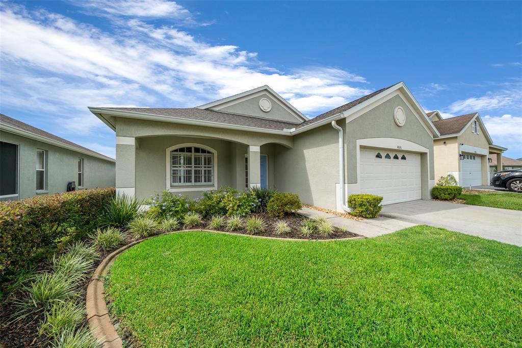 A single-story house with a beige stucco exterior, a two-car garage, and a landscaped yard — 14316 HOLLY HAMMOCK LANE, BROOKSVILLE, FL