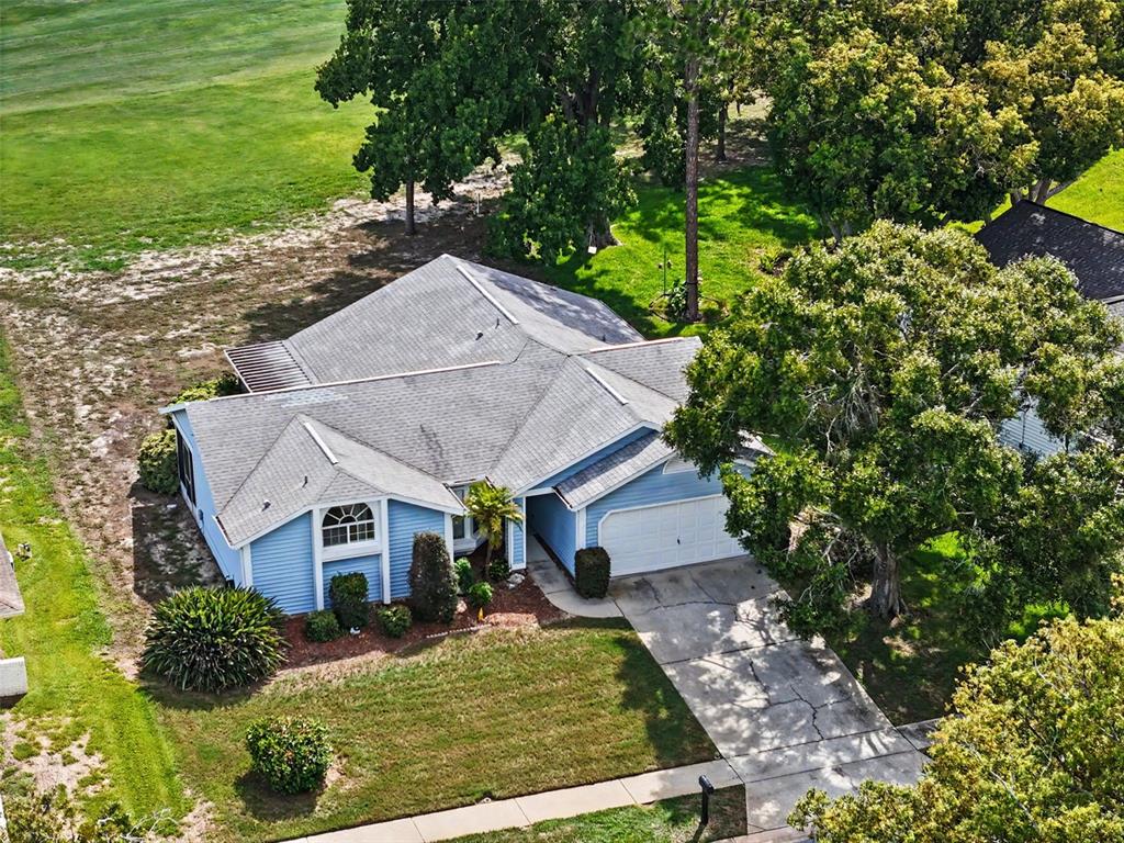 An aerial view shows a blue, single-story house with a shingled roof and a driveway — 13105 WESTERN CIRCLE, HUDSON, FL
