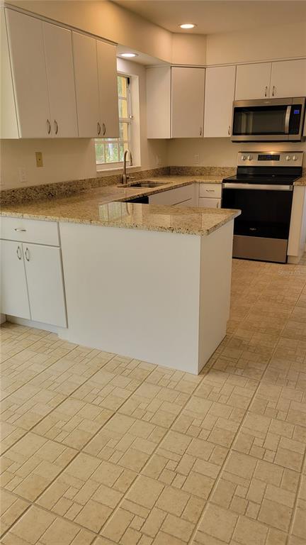 A kitchen features white cabinetry, granite countertops, stainless steel appliances, and light-colored tiled flooring — 3520 57TH AVENUE CIRCLE W UNIT 10, BRADENTON, FL
