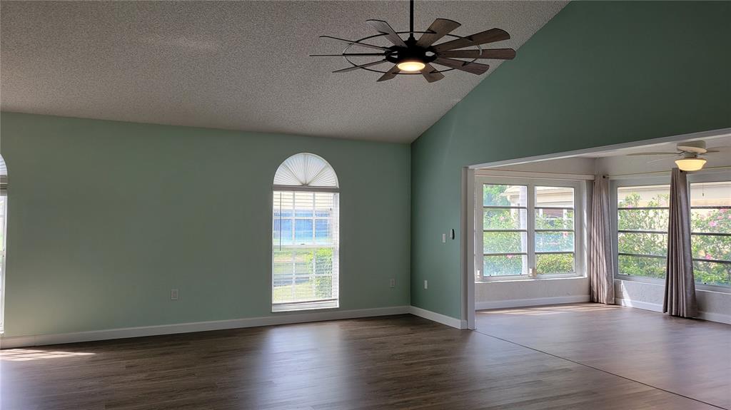 A living room with light green walls, vaulted ceilings, a ceiling fan, and wood-look flooring — 3520 57TH AVENUE CIRCLE W UNIT 10, BRADENTON, FL