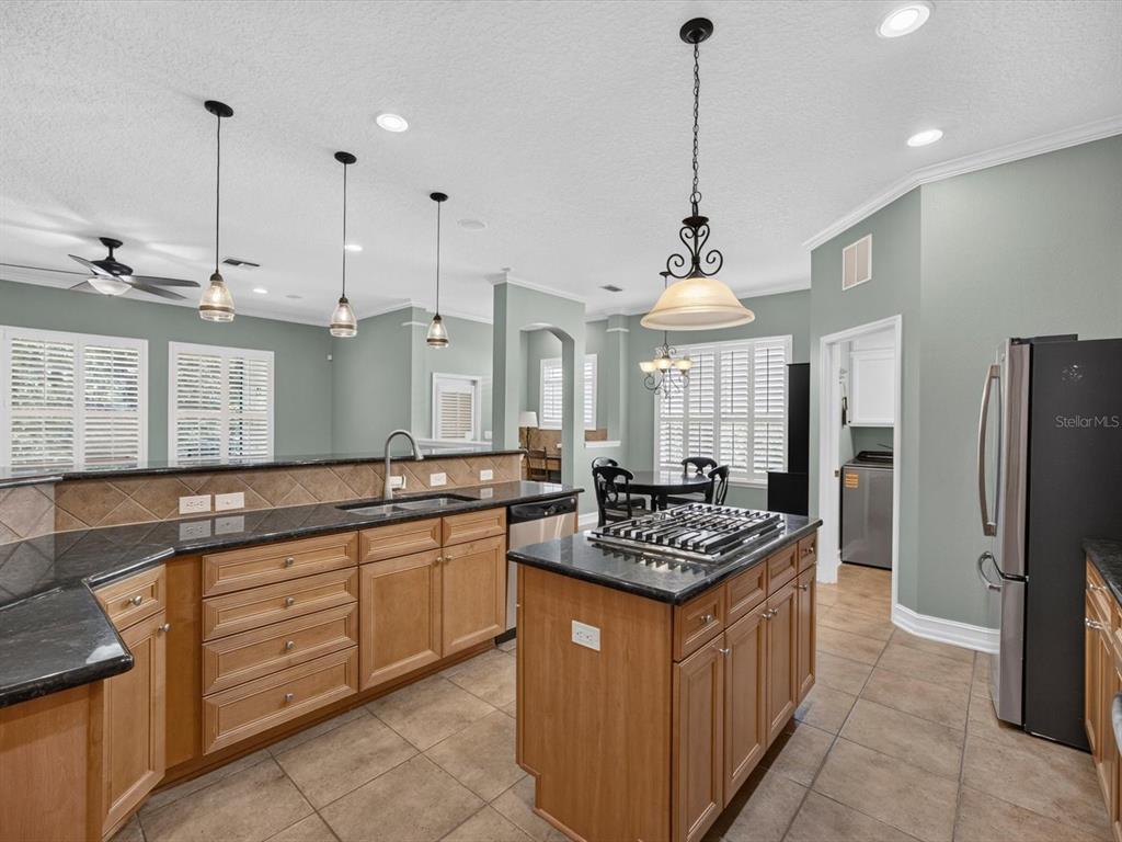 A kitchen features light wood cabinets, dark granite countertops, a center island, and pendant lighting — 112 BEDFORD COURT, DELAND, FL