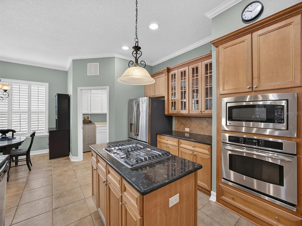 A kitchen features a central island with a gas cooktop, wood cabinetry, and stainless appliances — 112 BEDFORD COURT, DELAND, FL