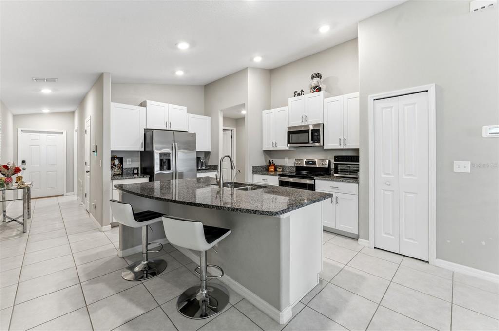 A kitchen features white cabinetry, granite countertops, a central island with bar stools, and tile flooring — 343 ARGYLL DRIVE, SPRING HILL, FL