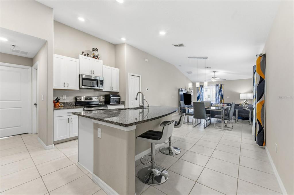 A kitchen with white cabinets, granite countertops, and a breakfast bar island opens to a dining area — 343 ARGYLL DRIVE, SPRING HILL, FL