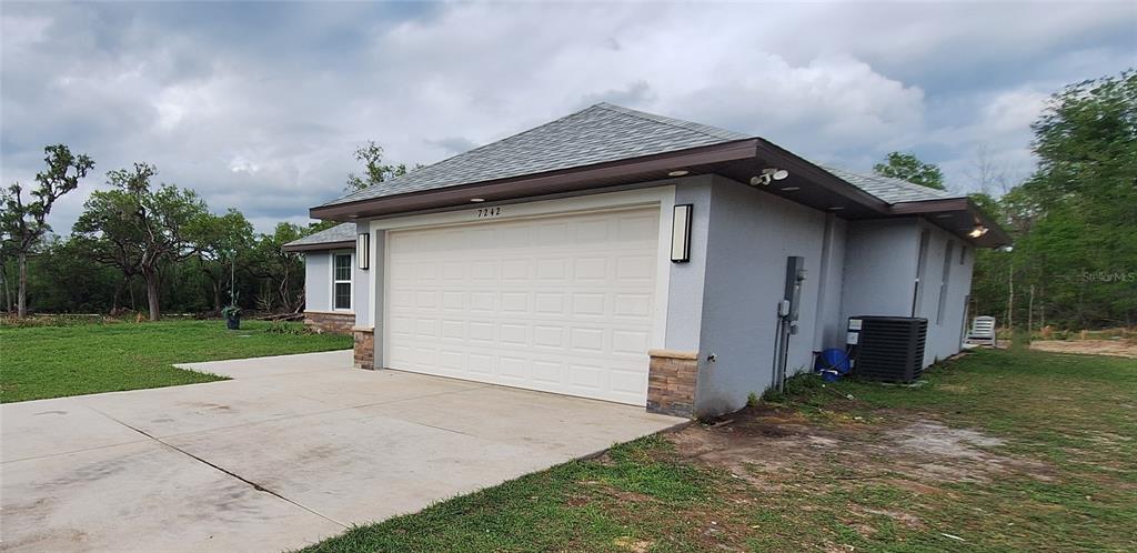 A gray house with a two-car garage and stone accents sits on a grassy lot — 7242 ELAINE DRIVE, WEBSTER, FL