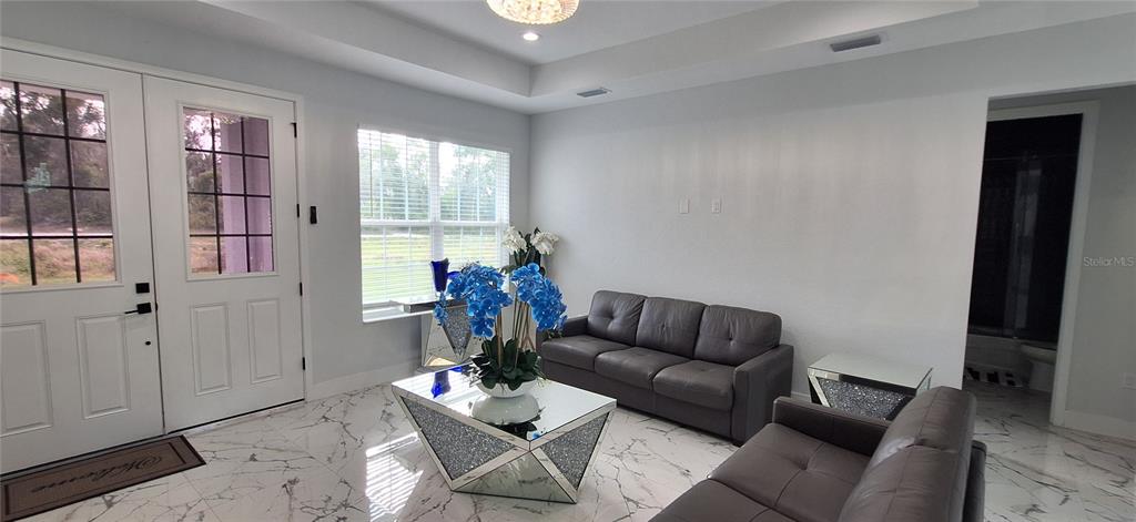 A living room features white walls, marble-patterned tile floors, and two gray leather sofas — 7242 ELAINE DRIVE, WEBSTER, FL