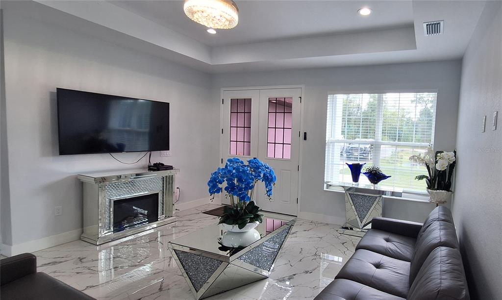 A living room features a mirrored fireplace, a glass coffee table, and white marble flooring — 7242 ELAINE DRIVE, WEBSTER, FL