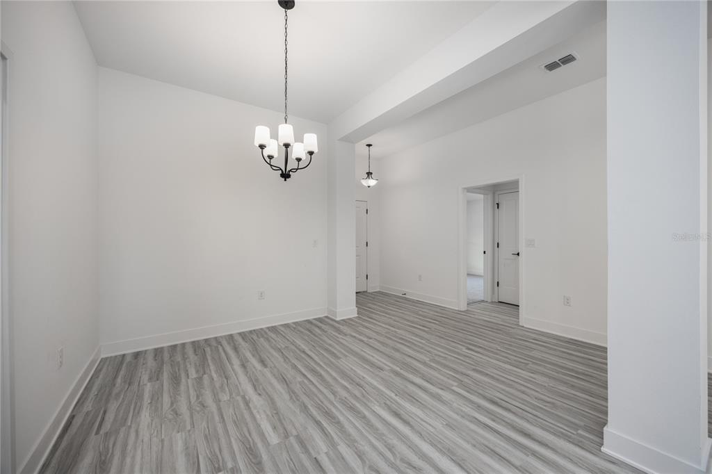 An empty dining area with a chandelier, white walls, and gray wood-look flooring — 581 SW BELLFLOWER DRIVE, LAKE CITY, FL