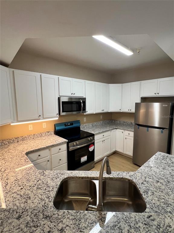 A kitchen features white cabinets, granite countertops, stainless steel appliances, and a double-basin sink — 5512 METROWEST BOULEVARD UNIT 12-201, ORLANDO, FL