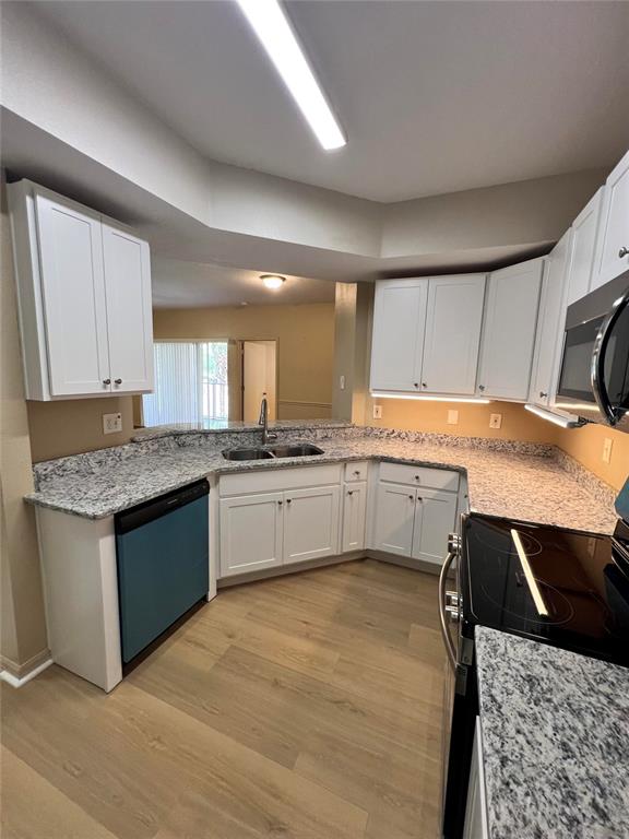 A kitchen features white cabinets, granite countertops, a stainless steel sink, and light wood flooring — 5512 METROWEST BOULEVARD UNIT 12-201, ORLANDO, FL