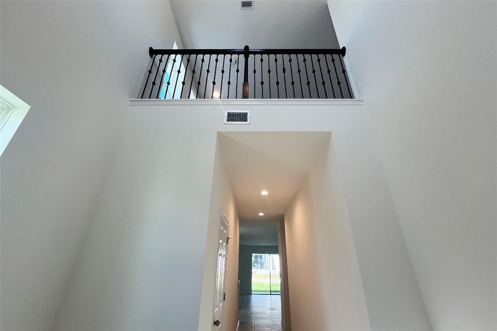 A high-ceilinged foyer features a dark metal railing overlooking a hallway with recessed lighting — 7052 ROLLING LEAF ROAD, GROVELAND, FL