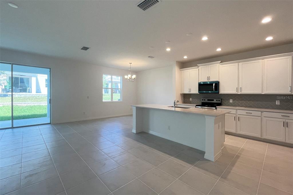 A kitchen with white cabinets, a central island, and tile flooring opens to a dining area — 7052 ROLLING LEAF ROAD, GROVELAND, FL