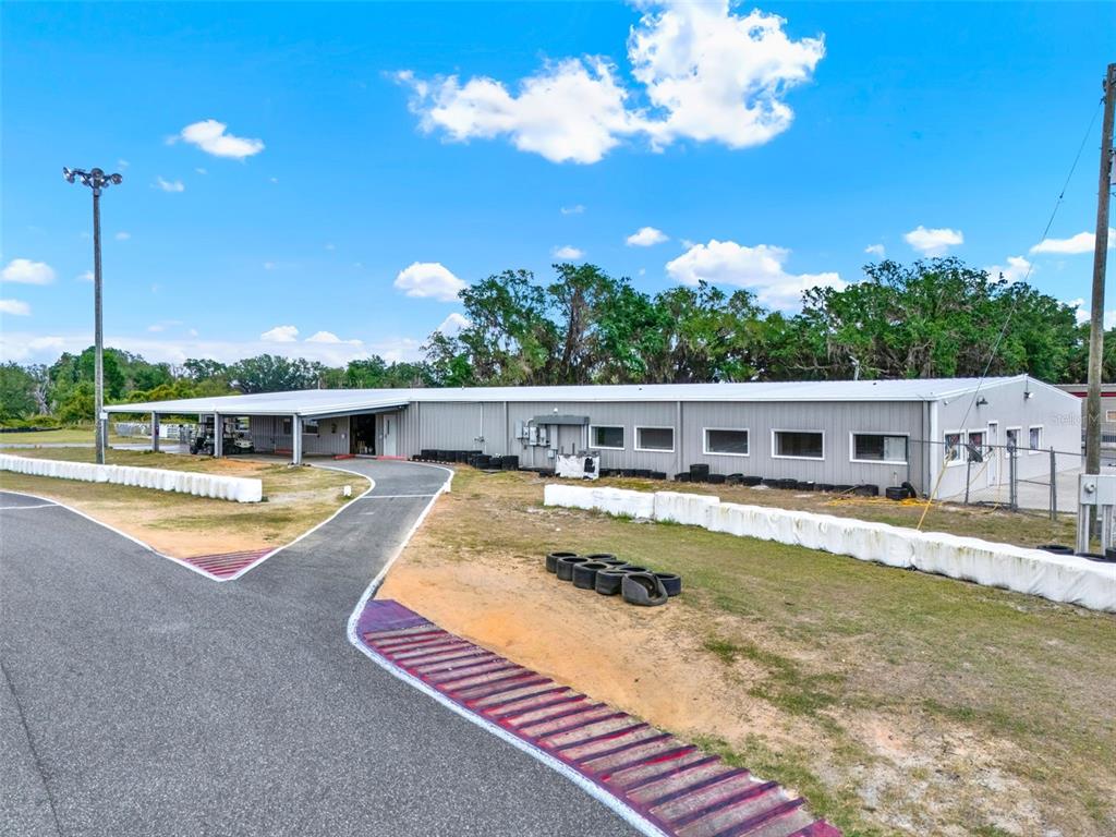 A long, single-story metal industrial building sits next to an asphalt track with tire barriers — 5821 PIT ROAD, BUSHNELL, FL