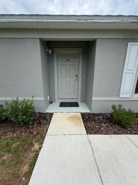 A concrete walkway leads to the front entrance of a house with gray stucco siding — 2776 SW 164TH STREET ROAD, OCALA, FL