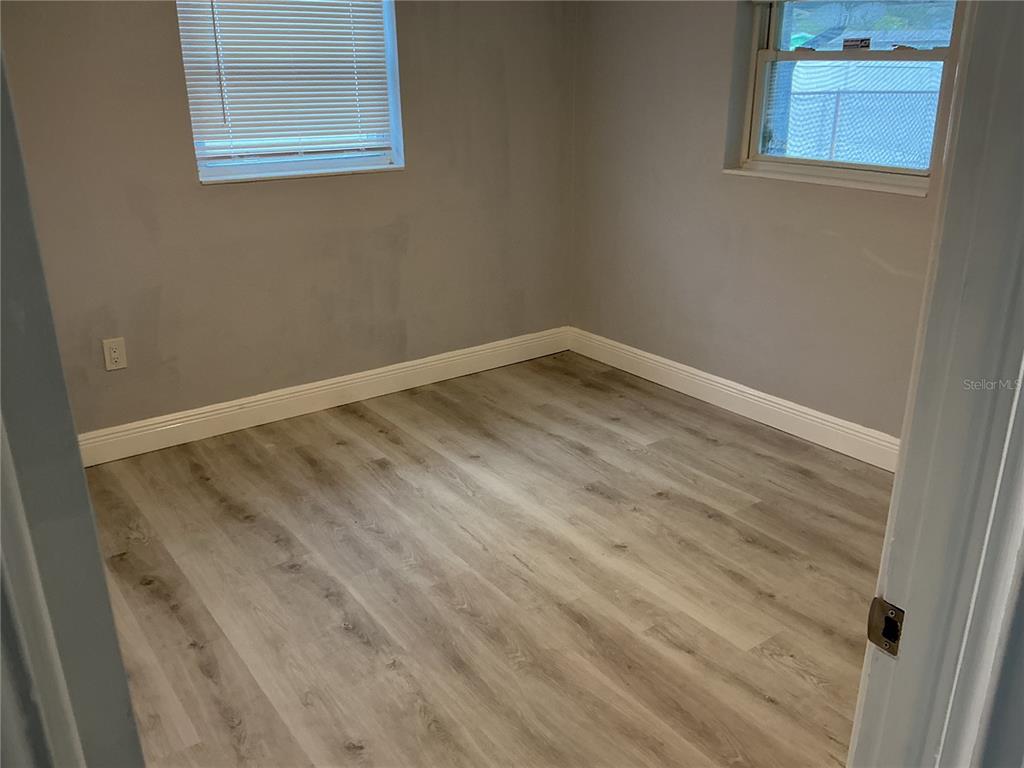 An empty bedroom features gray walls, light wood-look flooring, white baseboards, and two windows — 4660 71ST AVENUE N, PINELLAS PARK, FL