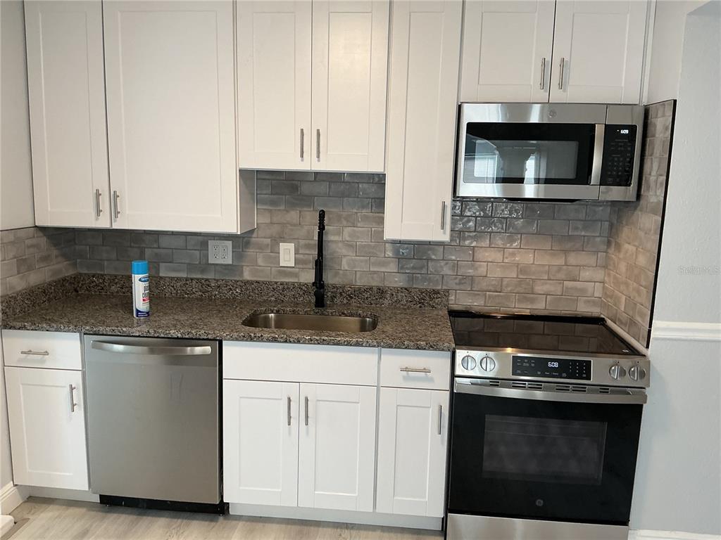 A kitchen features white cabinets, granite countertops, a gray subway tile backsplash, and stainless appliances — 4660 71ST AVENUE N, PINELLAS PARK, FL
