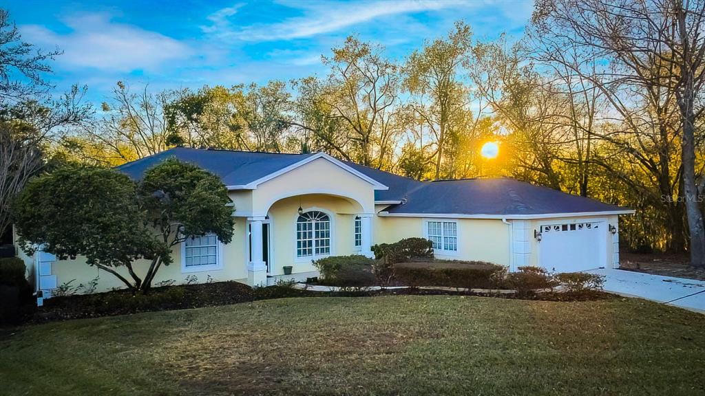 A single-story yellow house with a two-car garage sits on a lawn at sunset — 814 BRANTENBURG WAY, LUTZ, FL