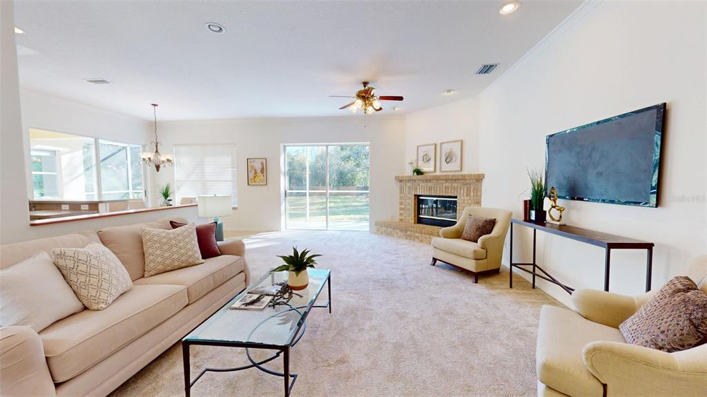 A living room features a brick fireplace, beige carpet, a sofa, and two armchairs — 814 BRANTENBURG WAY, LUTZ, FL