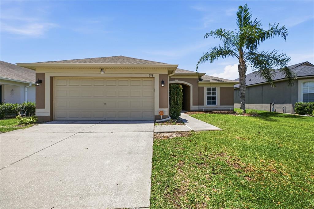 A single-story house with a beige stucco exterior, a two-car garage, and a palm tree — 698 WINTHROP DRIVE, SPRING HILL, FL