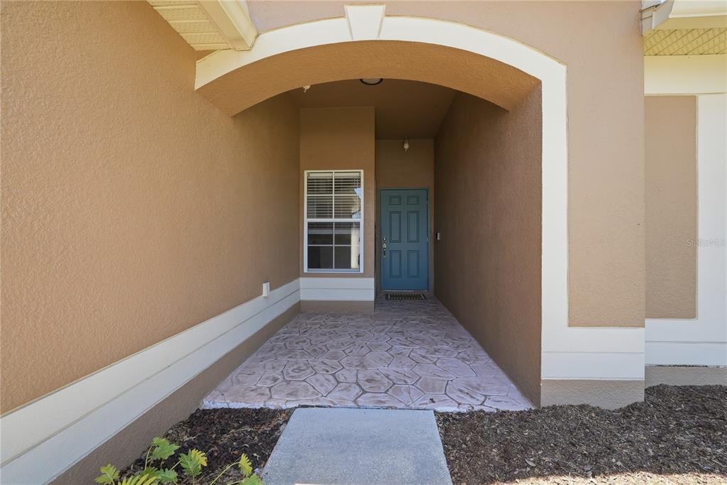 A covered entryway features a stamped concrete floor, a blue front door, and a window — 698 WINTHROP DRIVE, SPRING HILL, FL