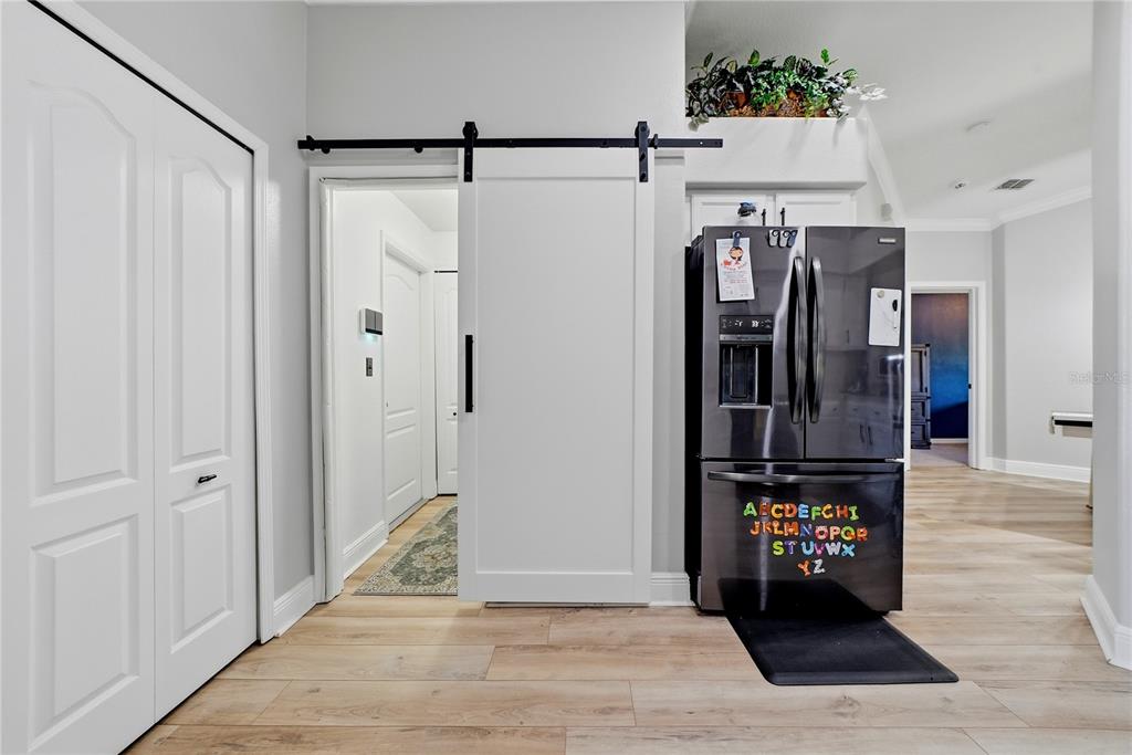 A kitchen features a white sliding barn door, a black refrigerator, and light wood flooring — 698 WINTHROP DRIVE, SPRING HILL, FL