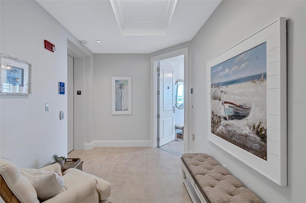 A bright hallway features tile flooring, a tufted bench, framed artwork, and an elevator entrance — 130 RIVIERA DUNES WAY UNIT 701, PALMETTO, FL