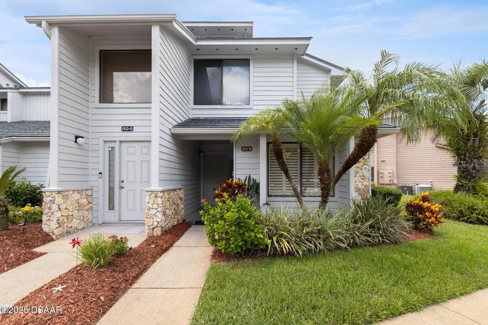 The exterior of a two-story residential building features light-colored siding, stone accents, and a palm tree — 150 BLUE HERON DRIVE UNIT B, DAYTONA BEACH, FL