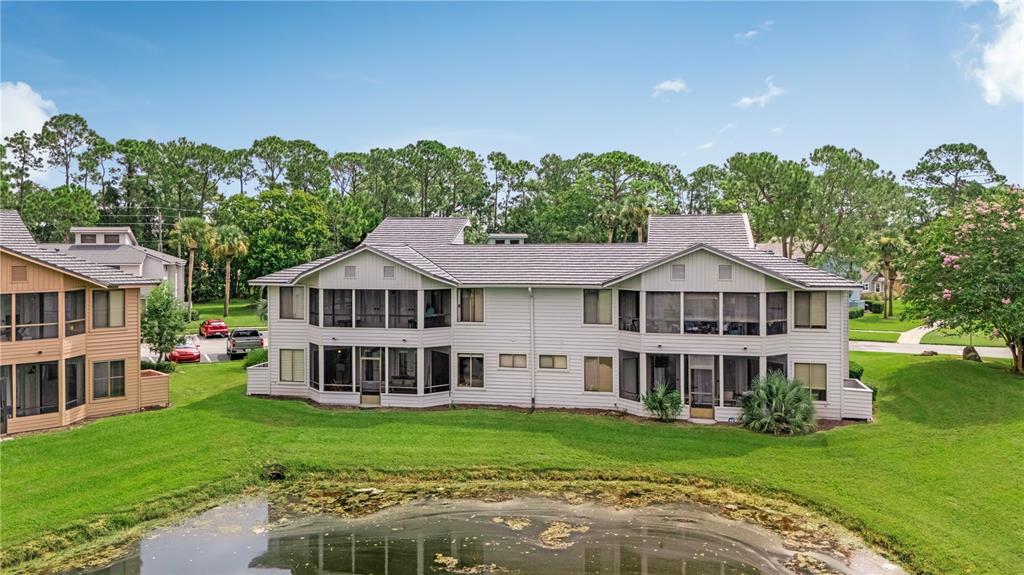 An exterior view of a two-story multi-family building with screened porches overlooking a pond — 150 BLUE HERON DRIVE UNIT B, DAYTONA BEACH, FL