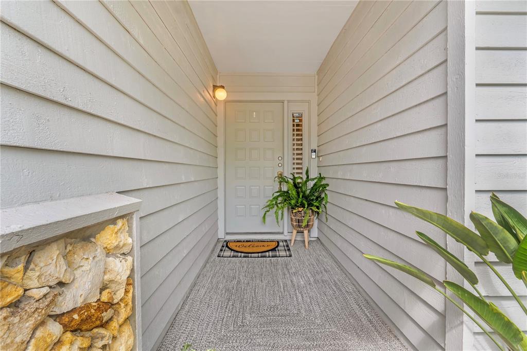 A covered entryway features light gray horizontal siding, a paneled door, and a stone planter — 150 BLUE HERON DRIVE UNIT B, DAYTONA BEACH, FL
