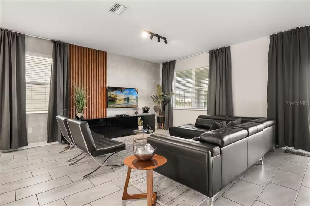 A modern living room features a wood-slat accent wall, black leather furniture, and tile flooring — 8882 CABOT CLIFFS DRIVE, DAVENPORT, FL