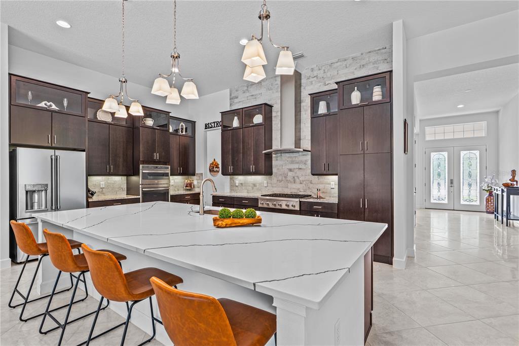 A modern kitchen features dark wood cabinets, a large white quartz island, and tile flooring — 214 ASHWOOD COURT, ORMOND BEACH, FL