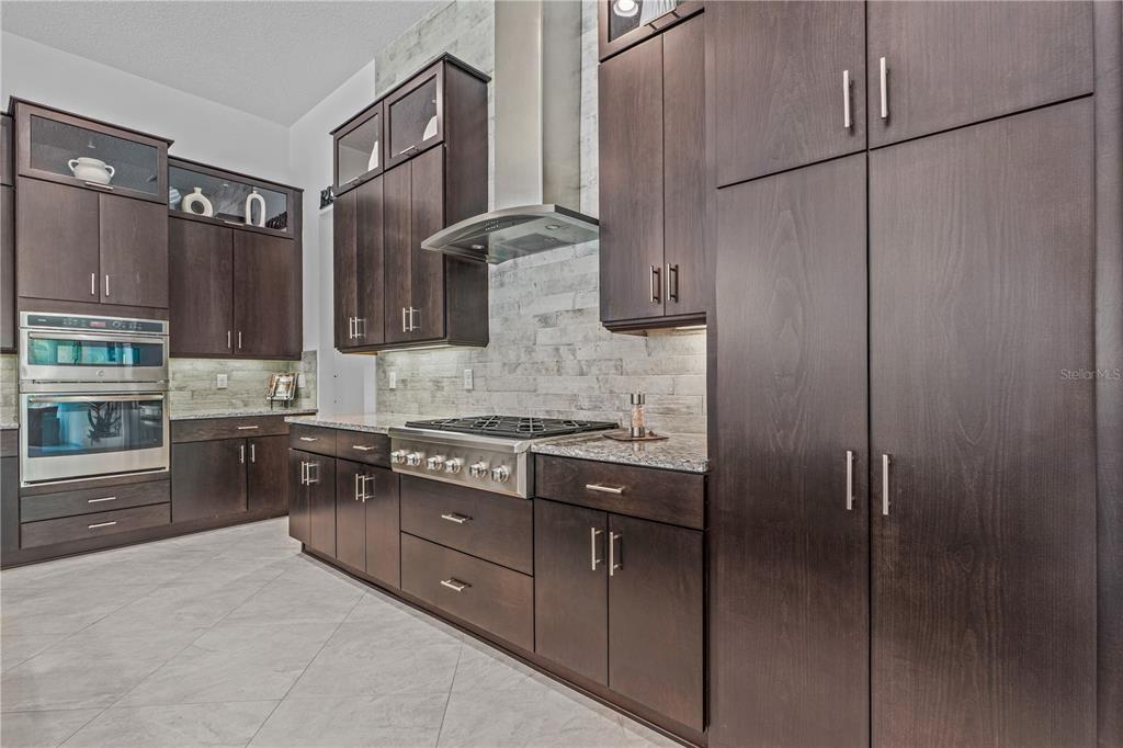 A modern kitchen features dark wood cabinetry, stainless steel appliances, and a light stone backsplash — 214 ASHWOOD COURT, ORMOND BEACH, FL