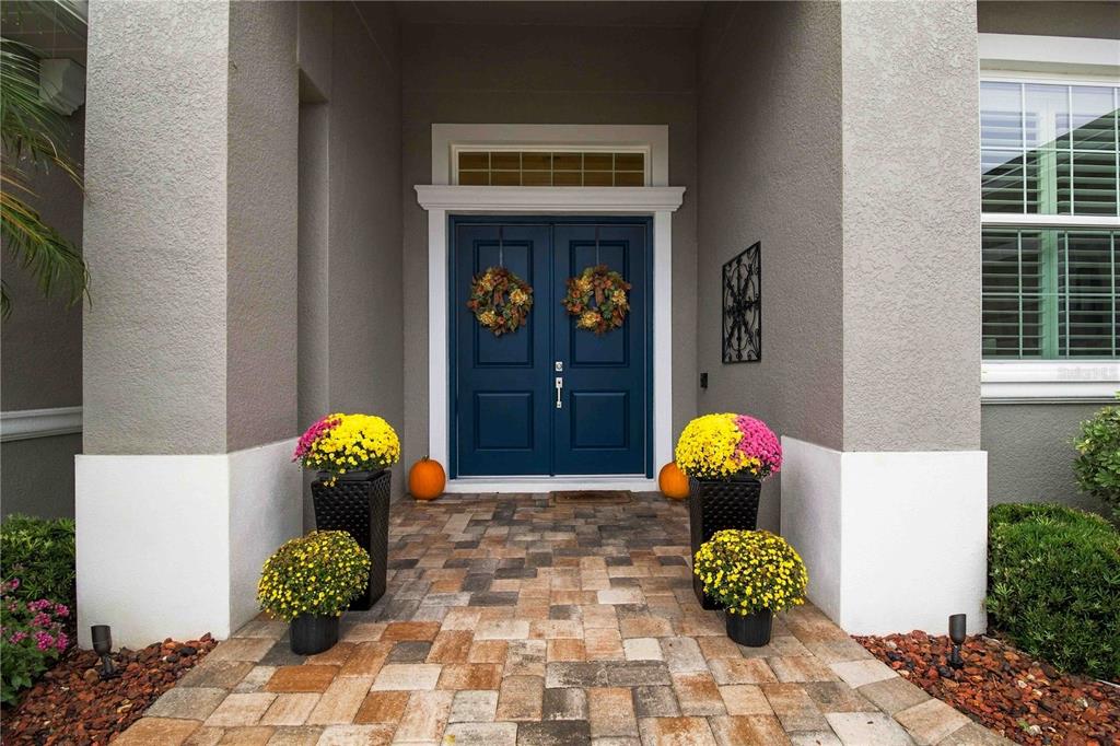 A blue double front door with fall wreaths and potted flowers sits on a paved porch — 1906 151ST TER E, PARRISH, FL