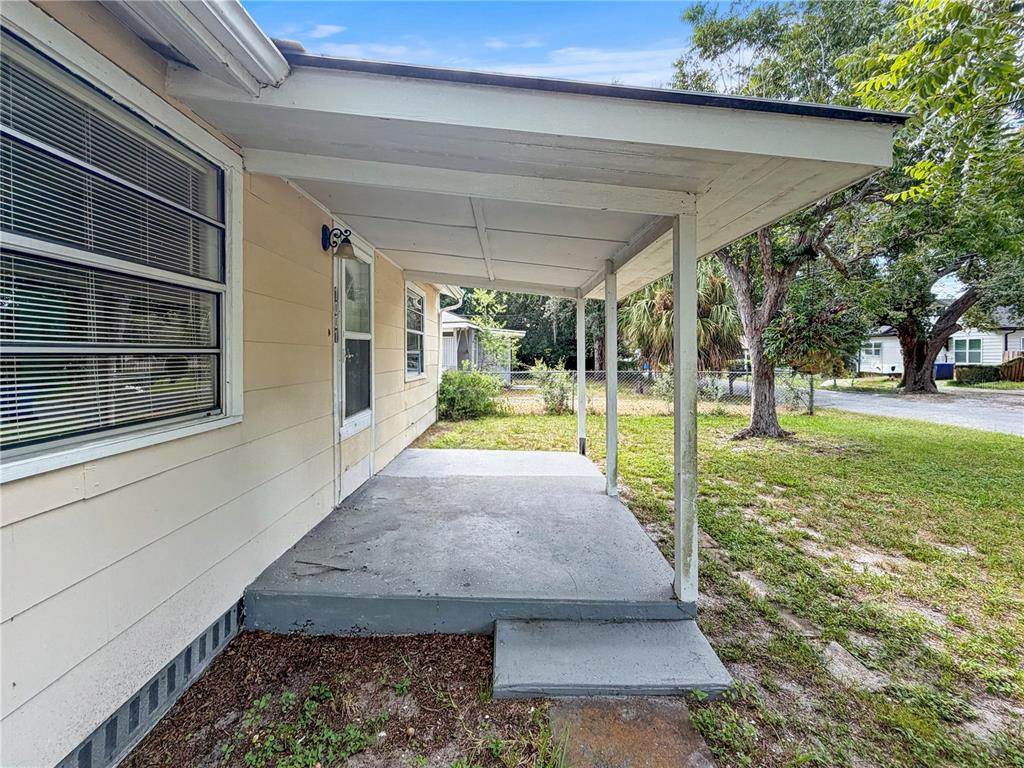 A covered concrete porch extends from the side of a light yellow house — 1455 10TH STREET NW, LARGO, FL