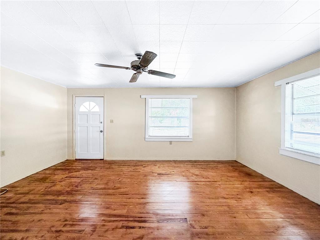 An empty room with hardwood floors, a ceiling fan, a white door, and two windows — 1455 10TH STREET NW, LARGO, FL