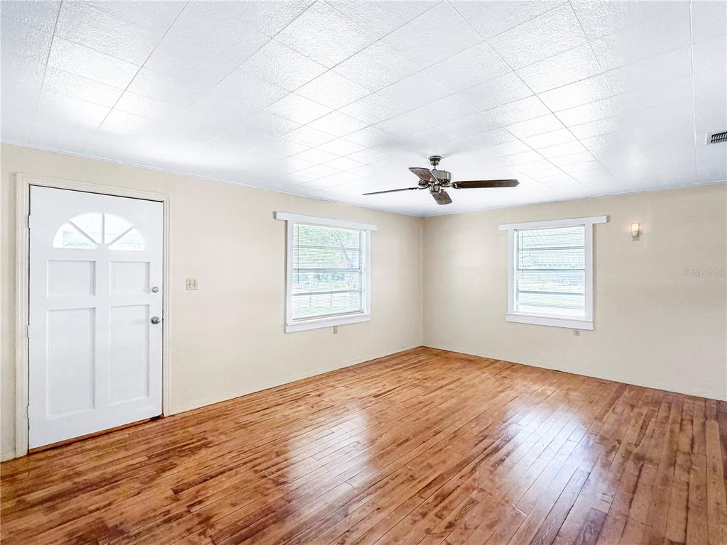 An empty room features hardwood floors, light-colored walls, a ceiling fan, and two windows — 1455 10TH STREET NW, LARGO, FL