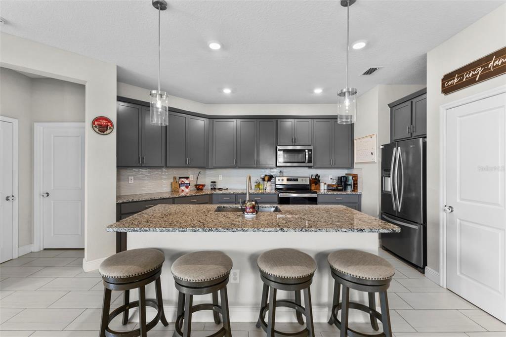 A kitchen features dark gray cabinetry, granite countertops, a central island with bar stools, and stainless steel appliances — 7434 35TH LANE E, SARASOTA, FL