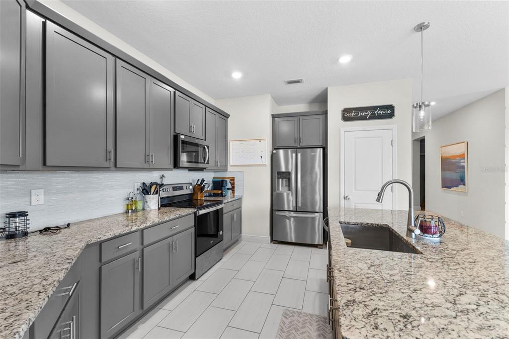 A kitchen features gray cabinets, granite countertops, stainless steel appliances, and a large island — 7434 35TH LANE E, SARASOTA, FL