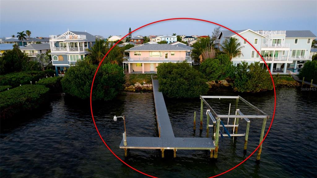 An aerial view shows a pink waterfront house with a long dock and boat lift — 2512 AVENUE A, BRADENTON BEACH, FL