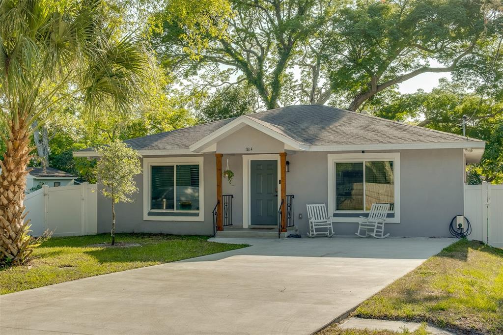 A gray single-story house with a concrete driveway, wooden porch posts, and two rocking chairs — 1814 SYLVAN DRIVE, CLEARWATER, FL
