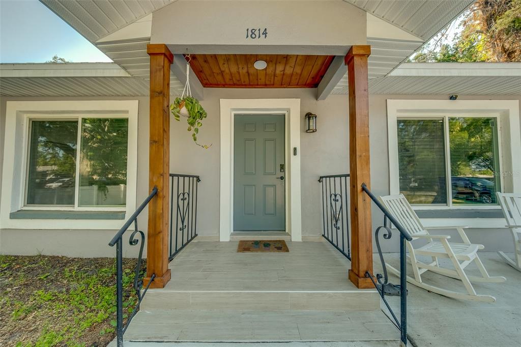 The front entrance of a house features a covered porch with wood posts and stairs — 1814 SYLVAN DRIVE, CLEARWATER, FL