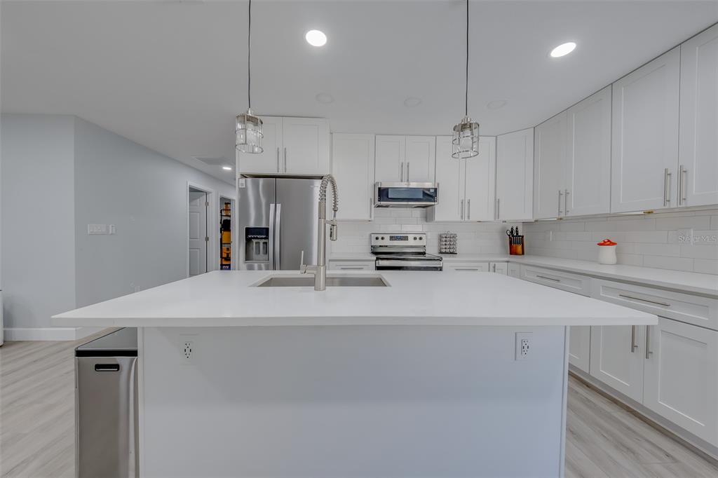 A modern kitchen features white cabinetry, a large central island, and stainless steel appliances — 1814 SYLVAN DRIVE, CLEARWATER, FL