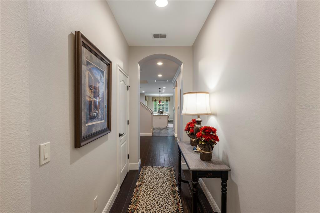 A hallway with dark wood floors, a console table, and a framed picture leads toward a kitchen — 8104 JAILENE DRIVE, WINDERMERE, FL