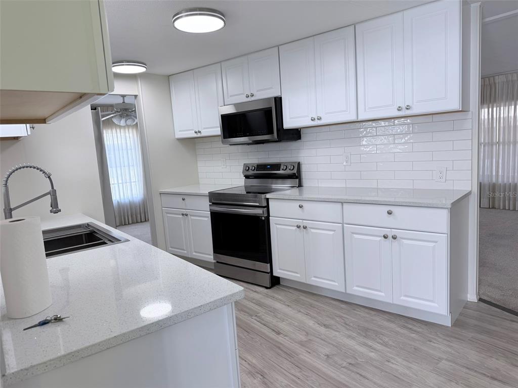 A galley kitchen features white cabinets, quartz countertops, stainless steel appliances, and light wood flooring — 2236 GONDOLA DRIVE, SARASOTA, FL