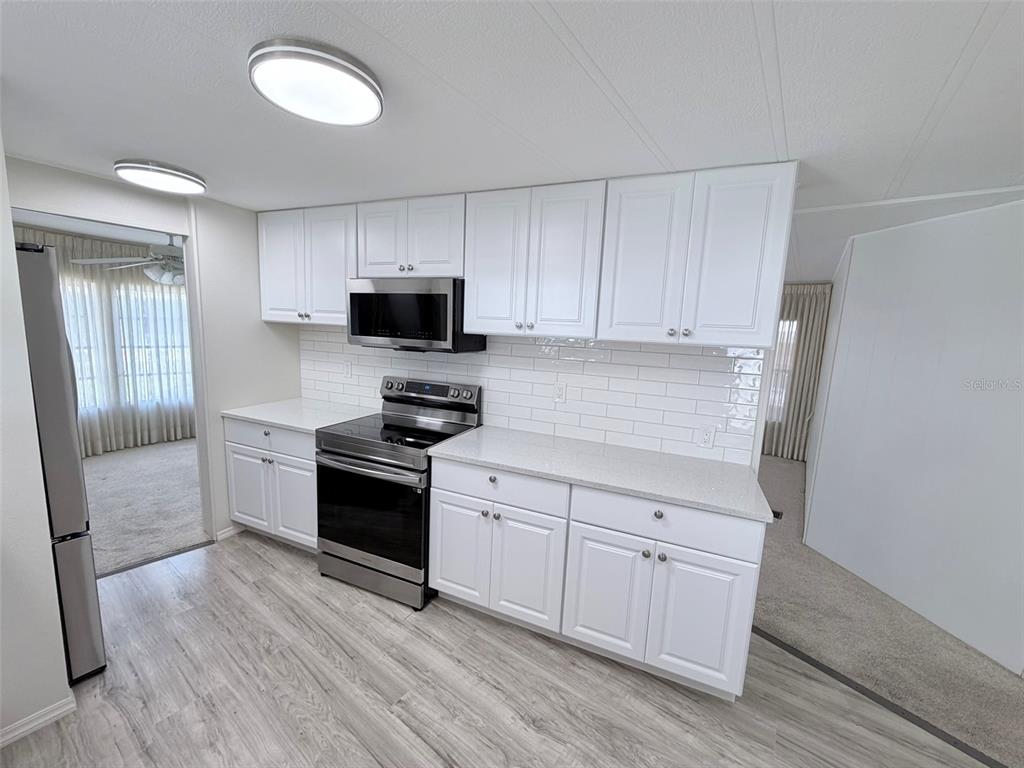 A kitchen features white cabinets, stainless steel appliances, quartz countertops, and a white subway tile backsplash — 2236 GONDOLA DRIVE, SARASOTA, FL