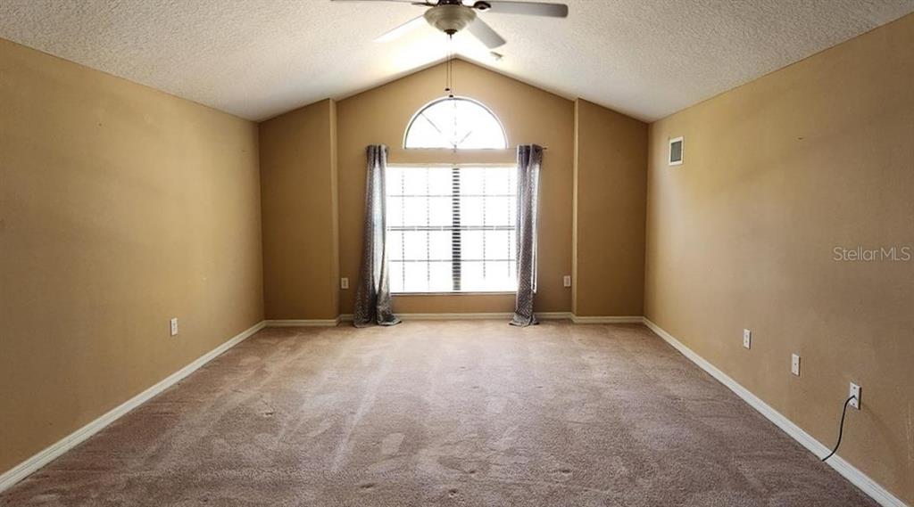 An empty bedroom features tan walls, beige carpeting, a vaulted ceiling, and a large arched window — 1134 IVEY LAKE DRIVE, ORANGE CITY, FL