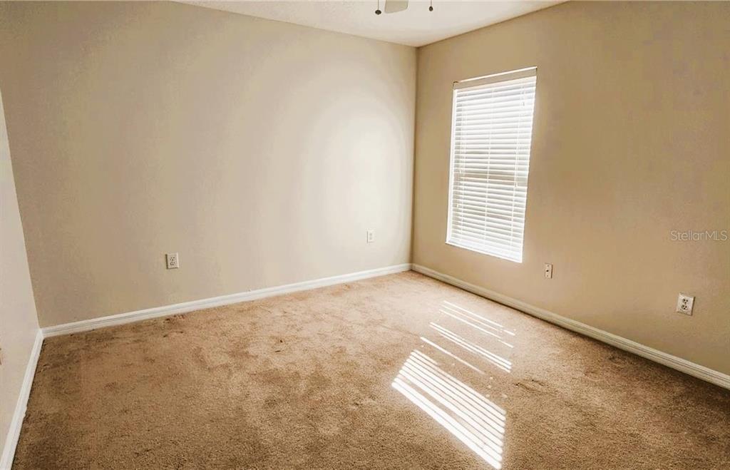 An empty bedroom features beige walls, tan carpeting, and a single window with white blinds — 1134 IVEY LAKE DRIVE, ORANGE CITY, FL
