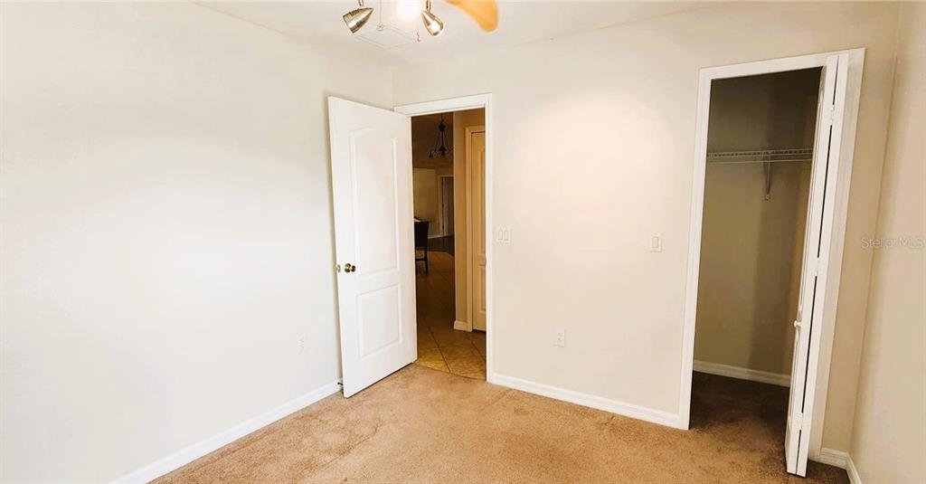 A bedroom with beige carpet, a ceiling fan, an open closet, and an open doorway — 1134 IVEY LAKE DRIVE, ORANGE CITY, FL